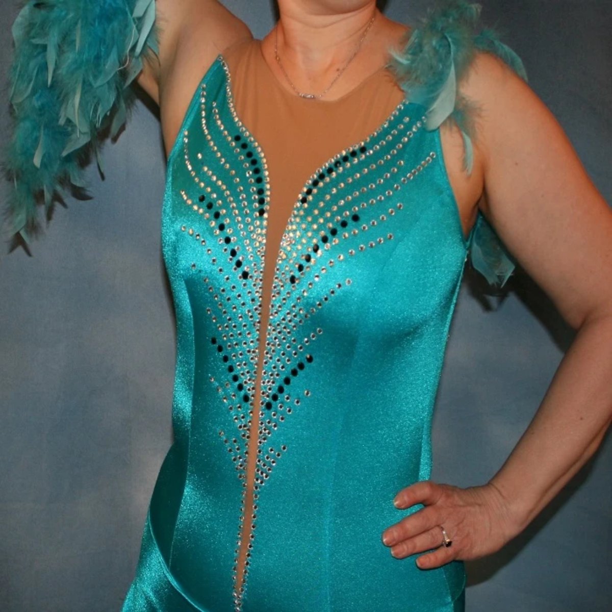 close upper view of Turquoise Latin/rhythm dance dress created in turquoise lycra on nude illusion, is embellished with crystal and jet black Swarovski rhinestones, with chandelle feathers and black spangles. The v styled skirt slits up high on both sides. Matching arm bands complete the look.