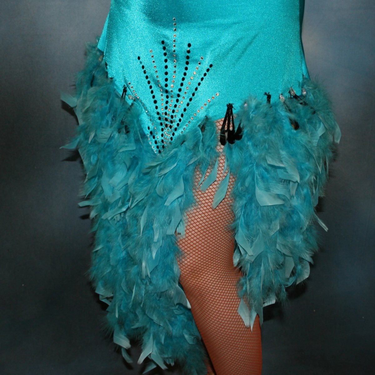 lower view of Turquoise Latin/rhythm dance dress created in turquoise lycra on nude illusion, is embellished with crystal and jet black Swarovski rhinestones, with chandelle feathers and black spangles. The v styled skirt slits up high on both sides. Matching arm bands complete the look.