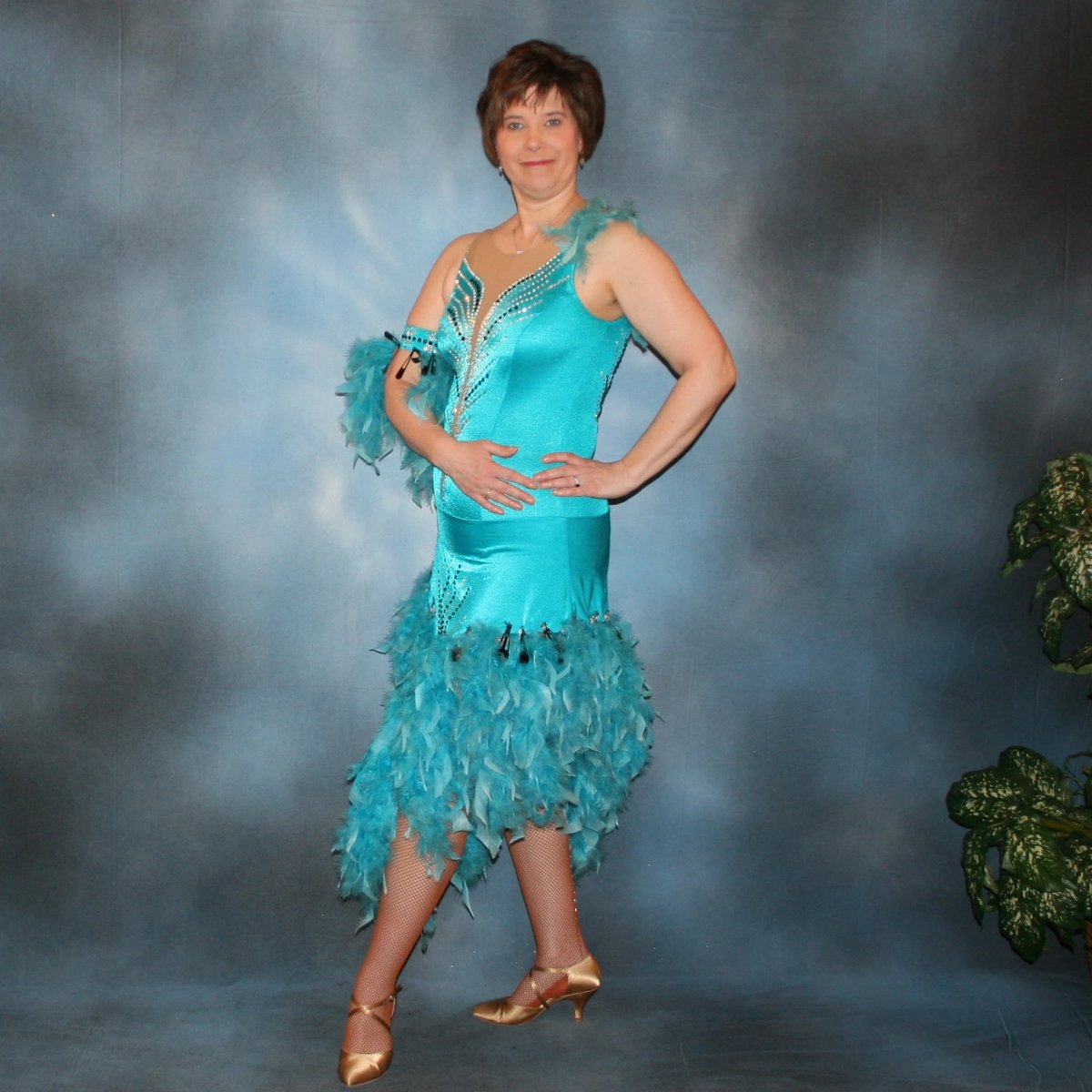 side view of Turquoise Latin/rhythm dance dress created in turquoise lycra on nude illusion, is embellished with crystal and jet black Swarovski rhinestones, with chandelle feathers and black spangles. The v styled skirt slits up high on both sides. Matching arm bands complete the look.