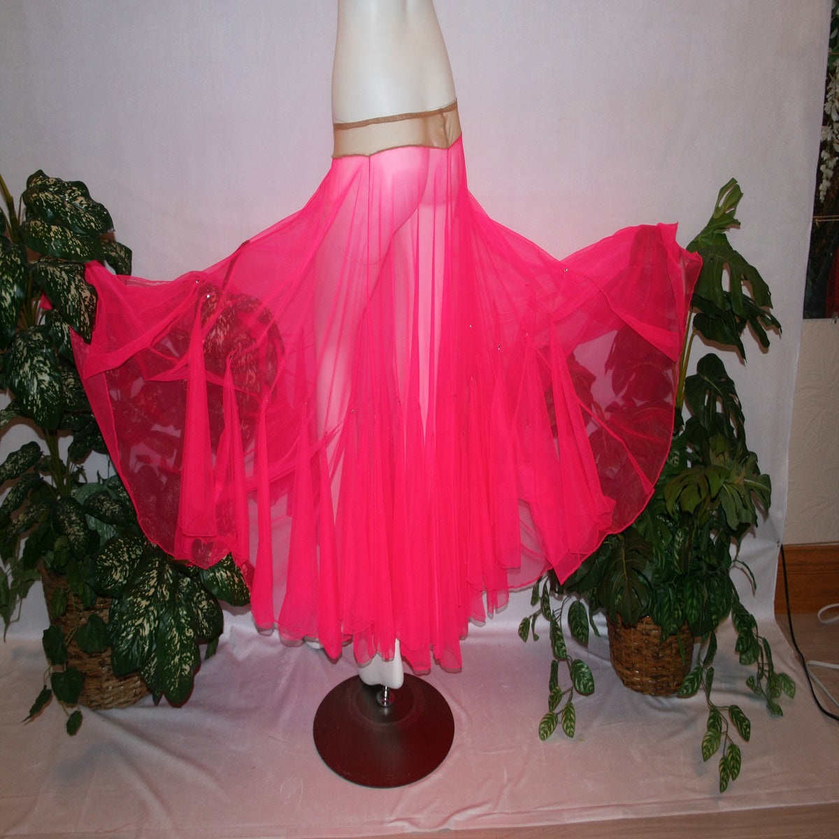 flaired side view of Hot pink ballroom skirt created with yards of hot pink sheer tricot with petal like floats around bottom embellished with tear drop Swarovski rhinestones.