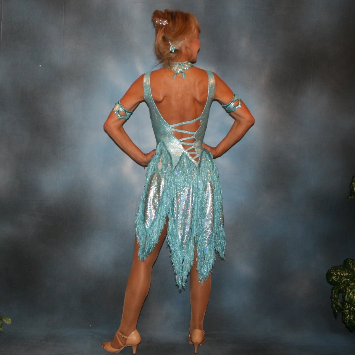 Crystal's Creations back view of Light turquoise Latin/rhythm dance dress created in turquoise hologram metallic lycra with hologram sequined fringe, is embellished with blue zircon Swarovski rhinestones, & features cutout detailing.