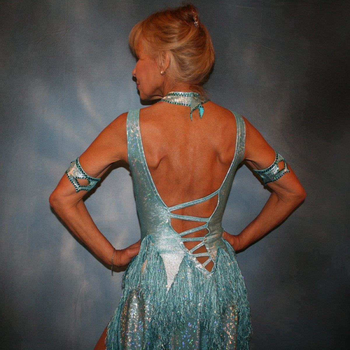Crystal's Creations close back view of Light turquoise Latin/rhythm dance dress created in turquoise hologram metallic lycra with hologram sequined fringe, is embellished with blue zircon Swarovski rhinestones, & features cutout detailing.