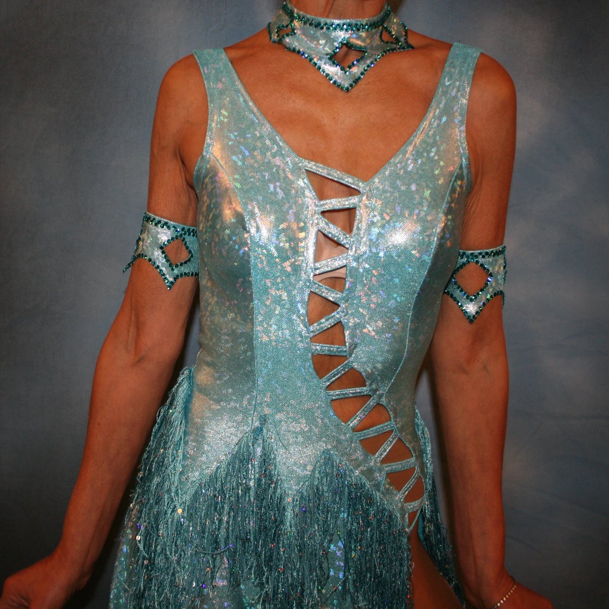 Crystal's Creations close up view of Light turquoise Latin/rhythm dance dress created in turquoise hologram metallic lycra with hologram sequined fringe, is embellished with blue zircon Swarovski rhinestones, & features cutout detailing.