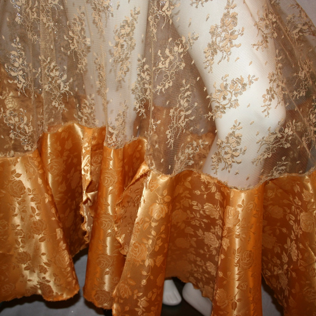 close up view of Ballroom skirt created on a nude illusion hip base of a gorgeous & delicate gold lace top flared section with gold brocade flounces at the bottom. 