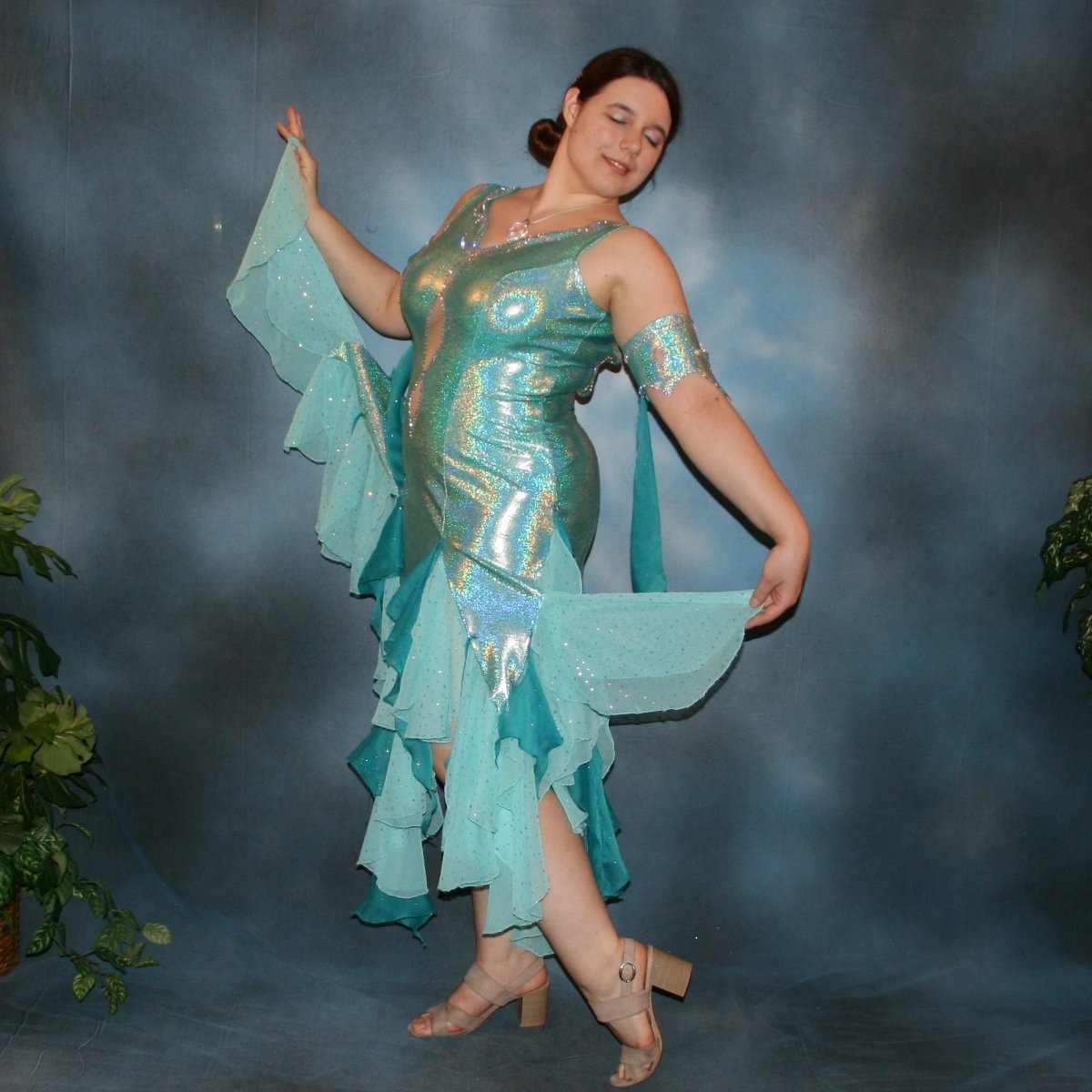 Crystal's Creations side view of Aqua Latin/rhythm dress created of gorgeous hologram base with flounces of aqua champagne sequin chiffon & teal glitter chiffon, embellished with CAB Swarovski stone work, with strap detailing on back. I envision this magical dress a gorgeous rumba, bolero or even a great solo dress for a waltz or foxtrot….or for an all around division.