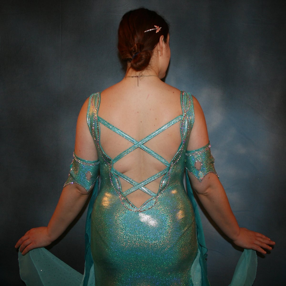 Crystal's Creations close up back view of Aqua Latin/rhythm dress created of gorgeous hologram base with flounces of aqua champagne sequin chiffon & teal glitter chiffon, embellished with CAB Swarovski stone work, with strap detailing on back. I envision this magical dress a gorgeous rumba, bolero or even a great solo dress for a waltz or foxtrot….or for an all around division.