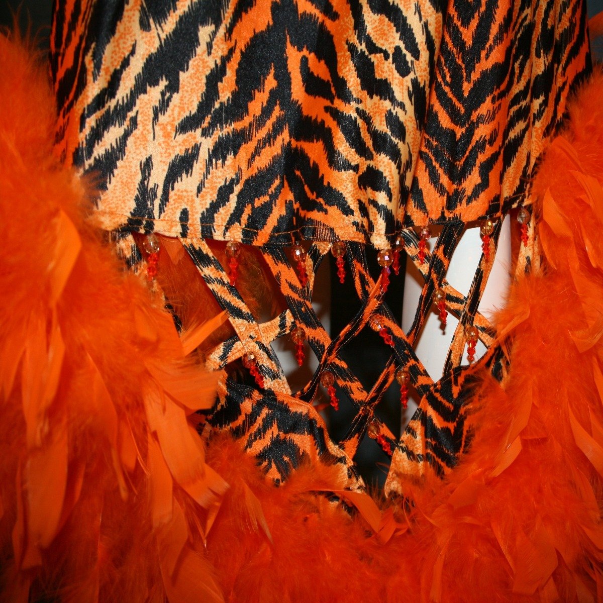 Crystal's Creations close up details view of  Tiger print & orange Latin/rhythm dress created of tiger print lycra & luxurious orange solid slinky has color blocking, lattice work detailing in front bodice, split sides & low back, as well as intriguing longer back skirting, adorned with orange chandelle feathers, also features detailed Swarovski rhinestone work!