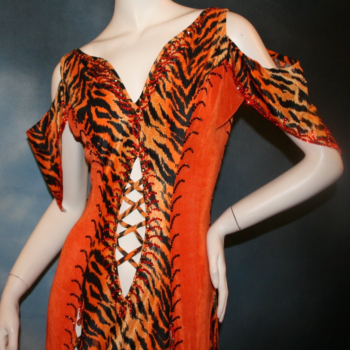 Crystal's Creations close up view of Tiger print & orange Latin/rhythm dress created of tiger print lycra & luxurious orange solid slinky has color blocking, lattice work detailing in front bodice, split sides & low back, as well as intriguing longer back skirting, adorned with orange chandelle feathers, also features detailed Swarovski rhinestone work!