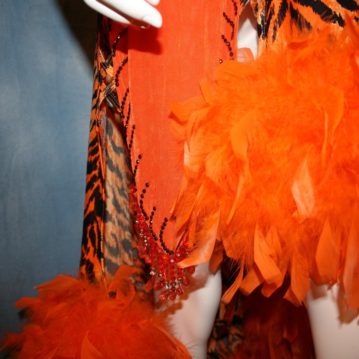 Crystal's Creations close up view of Tiger print & orange Latin/rhythm dress created of tiger print lycra & luxurious orange solid slinky has color blocking, lattice work detailing in front bodice, split sides & low back, as well as intriguing longer back skirting, adorned with orange chandelle feathers, also features detailed Swarovski rhinestone work!