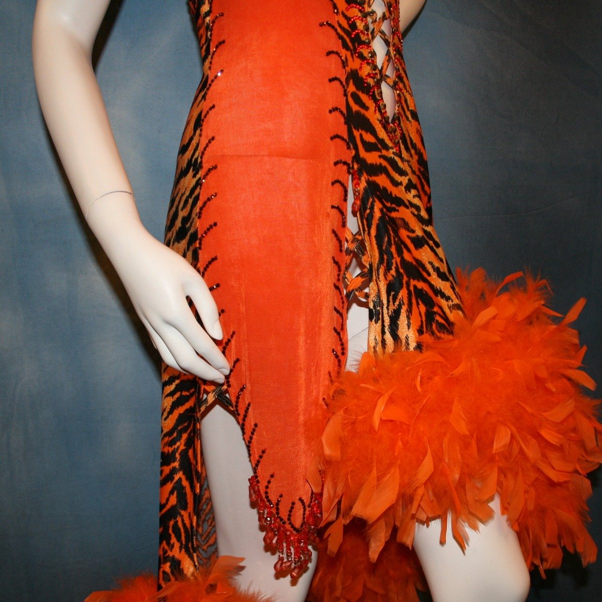 Crystal's Creations close up side view of Tiger print & orange Latin/rhythm dress created of tiger print lycra & luxurious orange solid slinky has color blocking, lattice work detailing in front bodice, split sides & low back, as well as intriguing longer back skirting, adorned with orange chandelle feathers, also features detailed Swarovski rhinestone work!