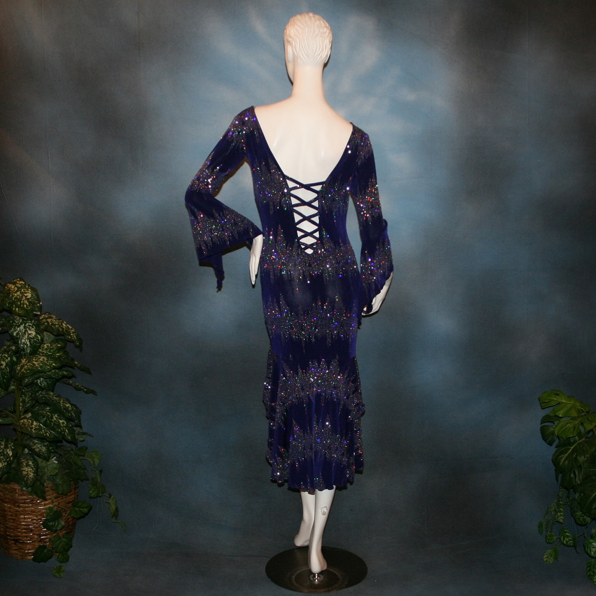 back view of Deep royal purple Latin/rhythm/tango dress created in deep royal purple glitter slinky with an awesome electrifying glitter pattern features long flaired sleeves, lattice strap detailing up the low back & a touch of hand beading in skirting slits.