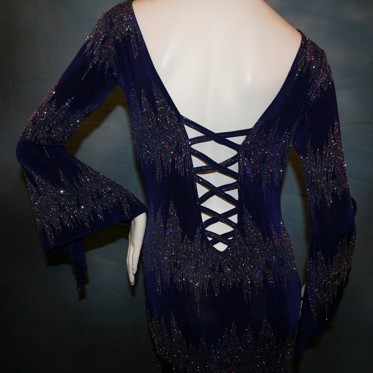 close back view of Deep royal purple Latin/rhythm/tango dress created in deep royal purple glitter slinky with an awesome electrifying glitter pattern features long flaired sleeves, lattice strap detailing up the low back & a touch of hand beading in skirting slits.
