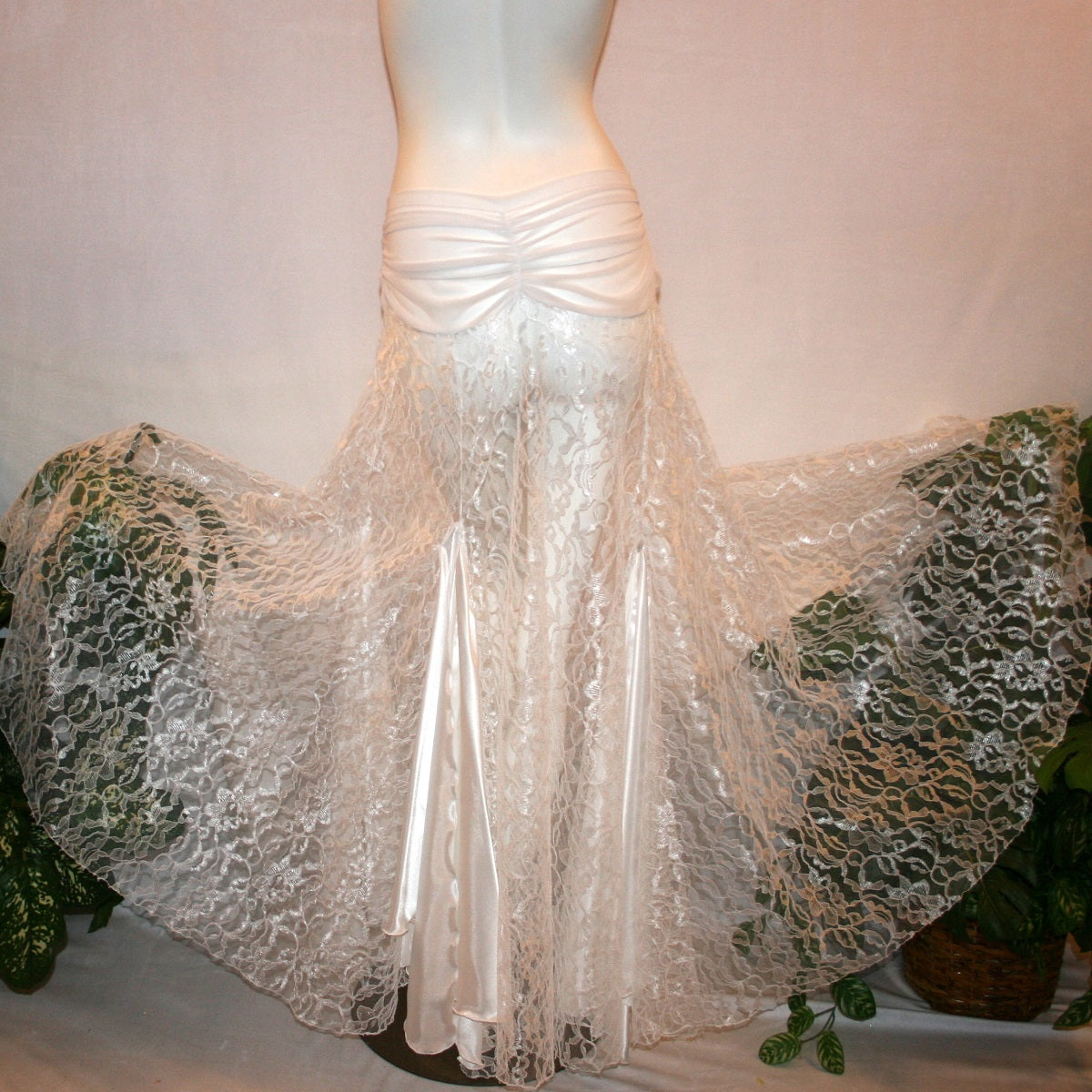 flaired back view of White ballroom skirt created of yards of white lace with a white sheer stretch mesh ruched hip band, has inset panels & floats of white stretch satin.