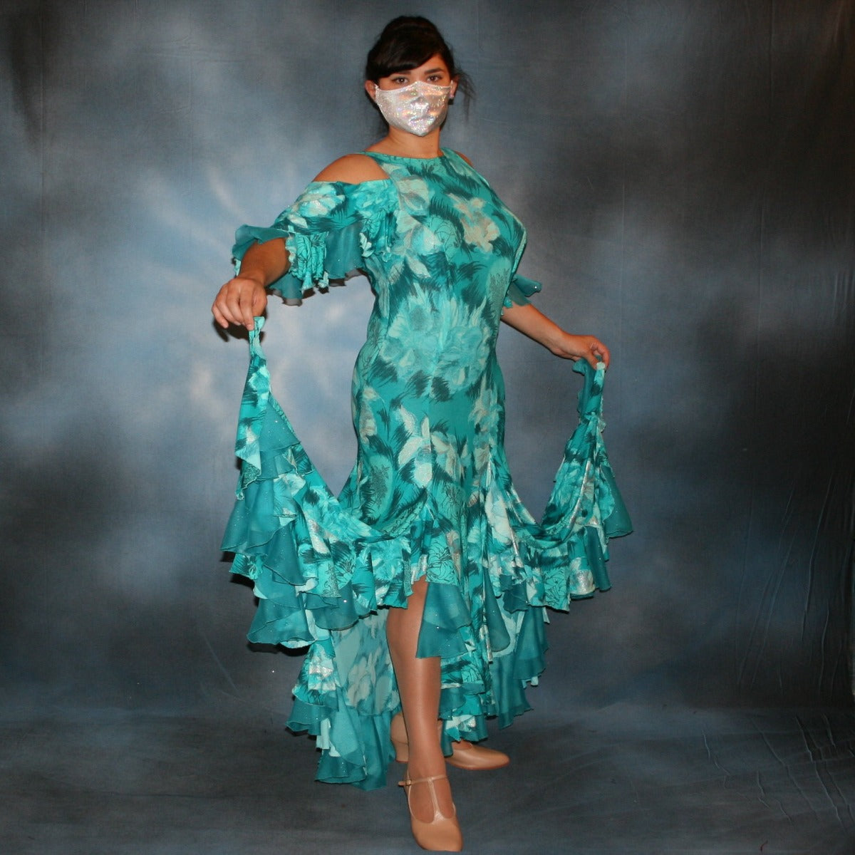 Crystal's Creations Gorgeous teal tropical print social ballroom dress created in tropical lycra print in shades of teal with a bit of silver sheen accents...absolutely gorgeous fabric! This social ballroom dress features very full skirting with 2 slits & oodles of flounces of the same teal tropical print lycra with intermittent flounces of teal glitter chiffon...along with draping, cold shoulder flounce sleeves...and a low back