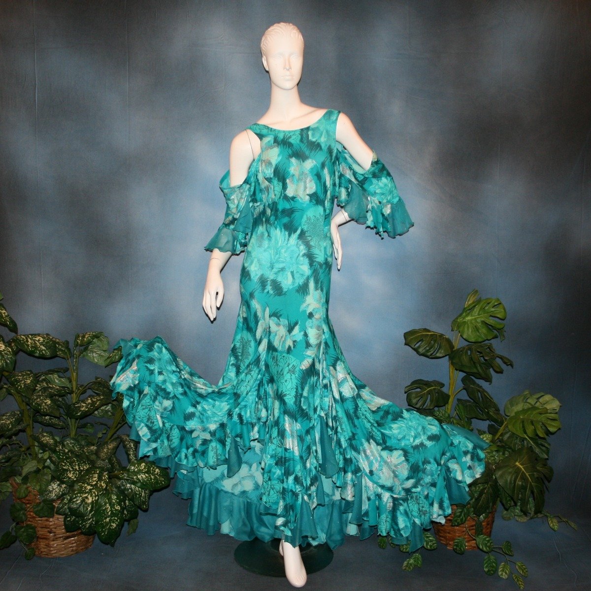 Gorgeous teal tropical print social ballroom dress created in tropical lycra print in shades of teal with a bit of silver sheen accents...absolutely gorgeous fabric! This social ballroom dress features very full skirting with 2 slits & oodles of flounces of the same teal tropical print lycra with intermittent flounces of teal glitter chiffon...along with draping, cold shoulder flounce sleeves...and a low back