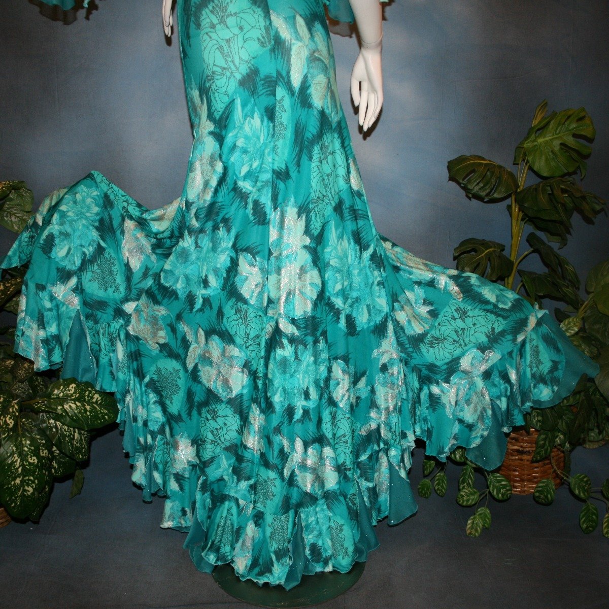 lower back view of Gorgeous teal tropical print social ballroom dress created in tropical lycra print in shades of teal with a bit of silver sheen accents...absolutely gorgeous fabric! This social ballroom dress features very full skirting with 2 slits & oodles of flounces of the same teal tropical print lycra with intermittent flounces of teal glitter chiffon...along with draping, cold shoulder flounce sleeves...and a low back