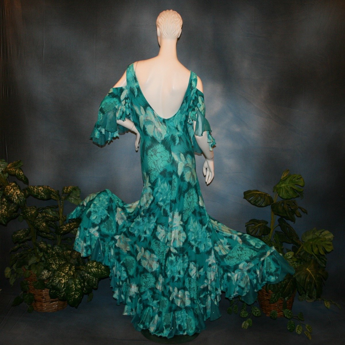 back view of Gorgeous teal tropical print social ballroom dress created in tropical lycra print in shades of teal with a bit of silver sheen accents...absolutely gorgeous fabric! This social ballroom dress features very full skirting with 2 slits & oodles of flounces of the same teal tropical print lycra with intermittent flounces of teal glitter chiffon...along with draping, cold shoulder flounce sleeves...and a low back