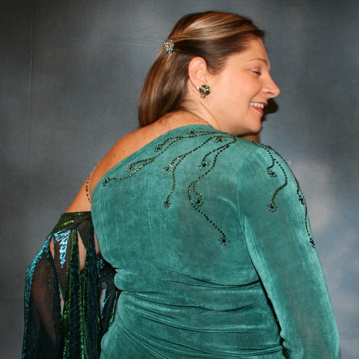 Crystal's Creations upper back view of Plus size teal Latin/rhythm dress or tango dress was created in luxurious teal solid slinky with iridescent floats & flounces plus a few champagne sequined flounces at bottom skirting. It is embellished with finely detailed Swarovski stonework in blue zircon, blue zircon AB and emerald green