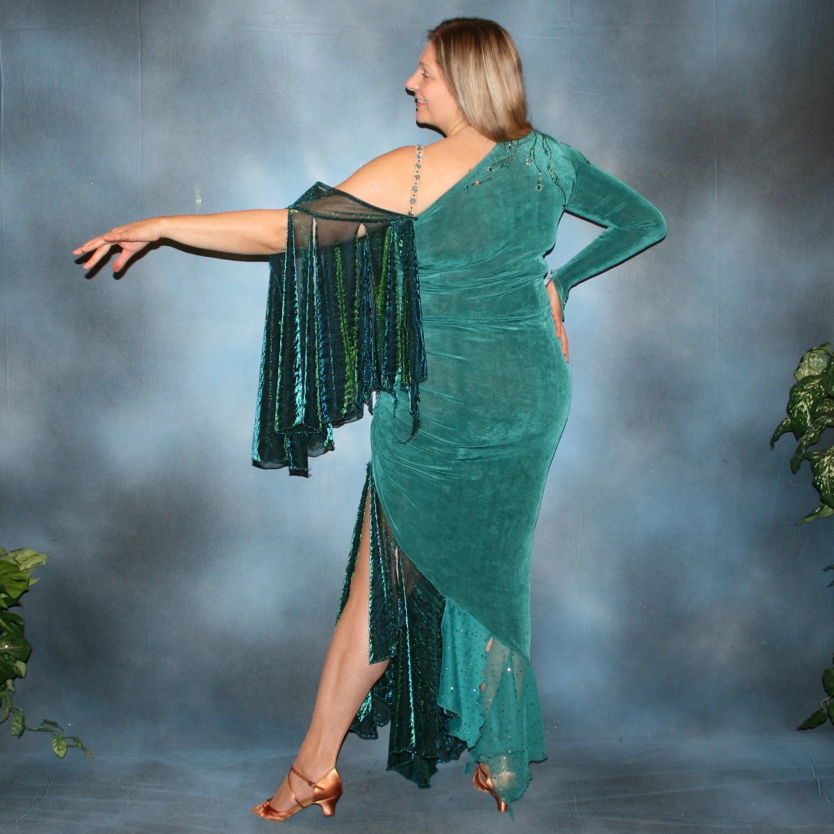 Crystal's Creations left back view of Plus size teal Latin/rhythm dress or tango dress was created in luxurious teal solid slinky with iridescent floats & flounces plus a few champagne sequined flounces at bottom skirting. It is embellished with finely detailed Swarovski stonework in blue zircon, blue zircon AB and emerald green