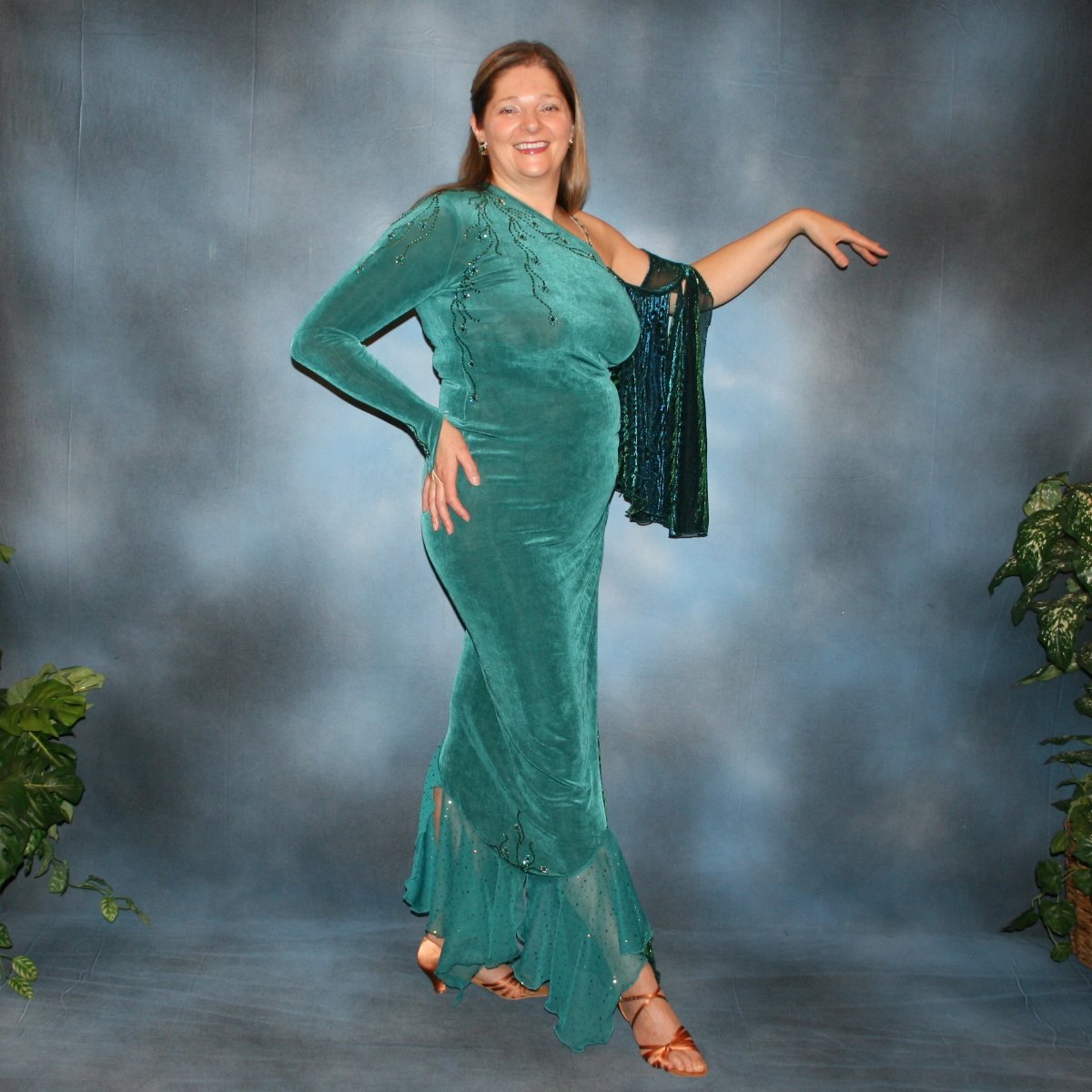 Crystal's Creations side view of Plus size teal Latin/rhythm dress or tango dress was created in luxurious teal solid slinky with iridescent floats & flounces plus a few champagne sequined flounces at bottom skirting. It is embellished with finely detailed Swarovski stonework in blue zircon, blue zircon AB and emerald. green