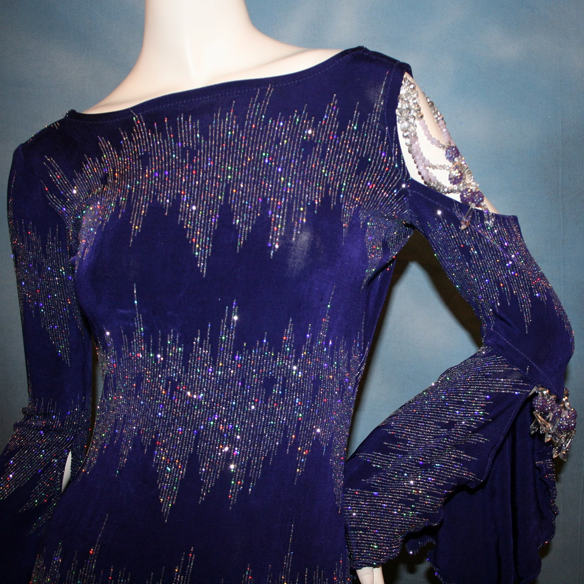 close up front view of Deep royal purple Latin/rhythm/tango dress created in deep royal purple glitter slinky with an awesome electrifying glitter pattern features one longe sleeve, with flair at the bottom, & another very interesting cold shoulder detailed one with hand beading & a flaired flounce.