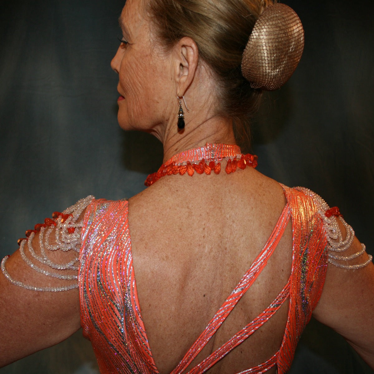 Crystal's Creations close up back view of Orange Latin/rhythm dress was created in orange & silver metallic print lycra with oodles of glitter organza flounces & accents, has back strap detailing, embellished with extensive Swarovski hand beading & has matching Swarovski hand beaded neckpiece.