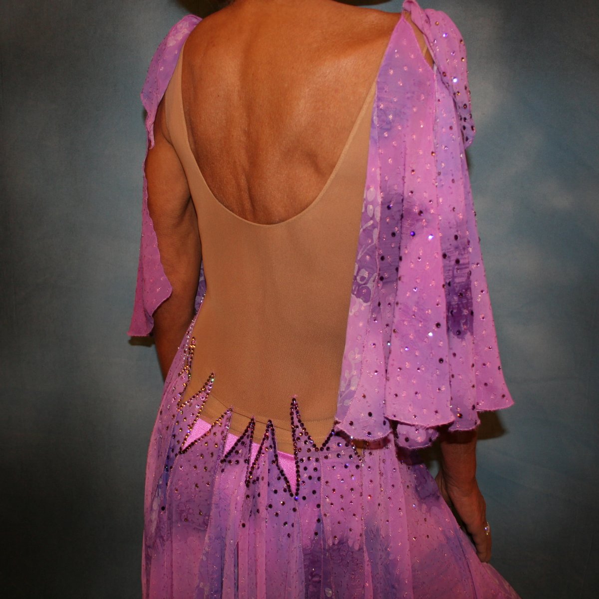 Crystal's Creations close up of backview of Orchid ballroom dress created in yards of a textured chiffon in shades of orchids & purples on a nude illusion base with floats & Swarovski stonework in gorgeous shades of orchids & purples.