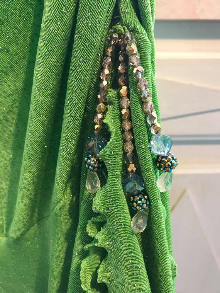 bottom bead detail of Apple green social Latin/rhythm dress was created of apple green glitter slinky, features ruching on the right side, long sleeves, scoop back, & full skirting with open side that has Swarovski hand beaded detail