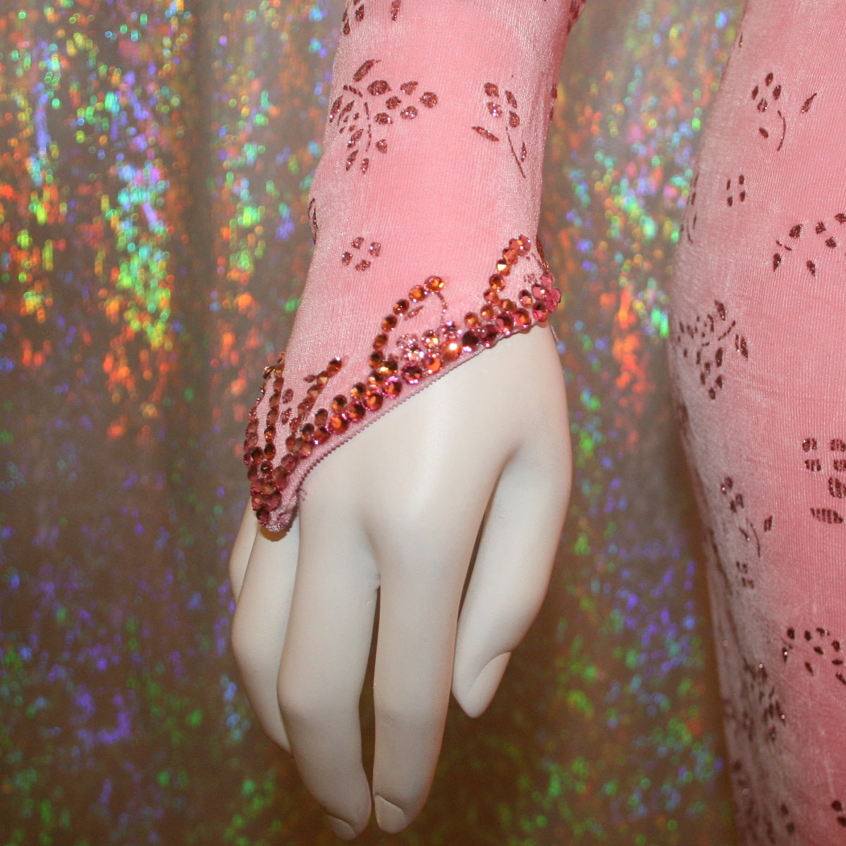 view of wrist detail on Delicate pink Latin-rhythm dress created of light pink glitter slinky with a delicate glitter flower pattern has sleek & classic lines, long sleeve on the right side with open lattice work detailing on the left side, embellished with Swarovski rhinestone work & hand beading