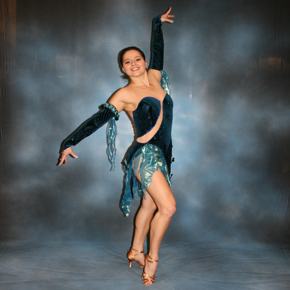 Crystal's Creations Latin/rhythm dance dress created of deep turquoise sea blue glitter stretch velvet fabric on nude illusion base is embellished with turquoise Swarovski rhinestones stones & lots of hand beading with sequin paillette bangles.