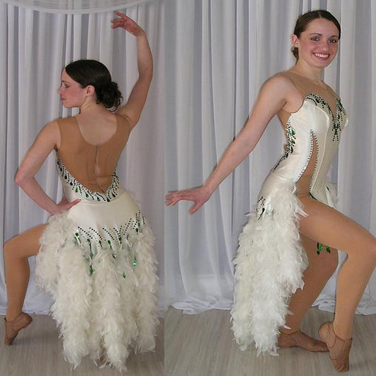 White Latin/rhythm dress created of white heavy lycra on a nude illusion base with white chandelle feathers & embellished with crystal and emerald green Swarovski rhinestone work. 