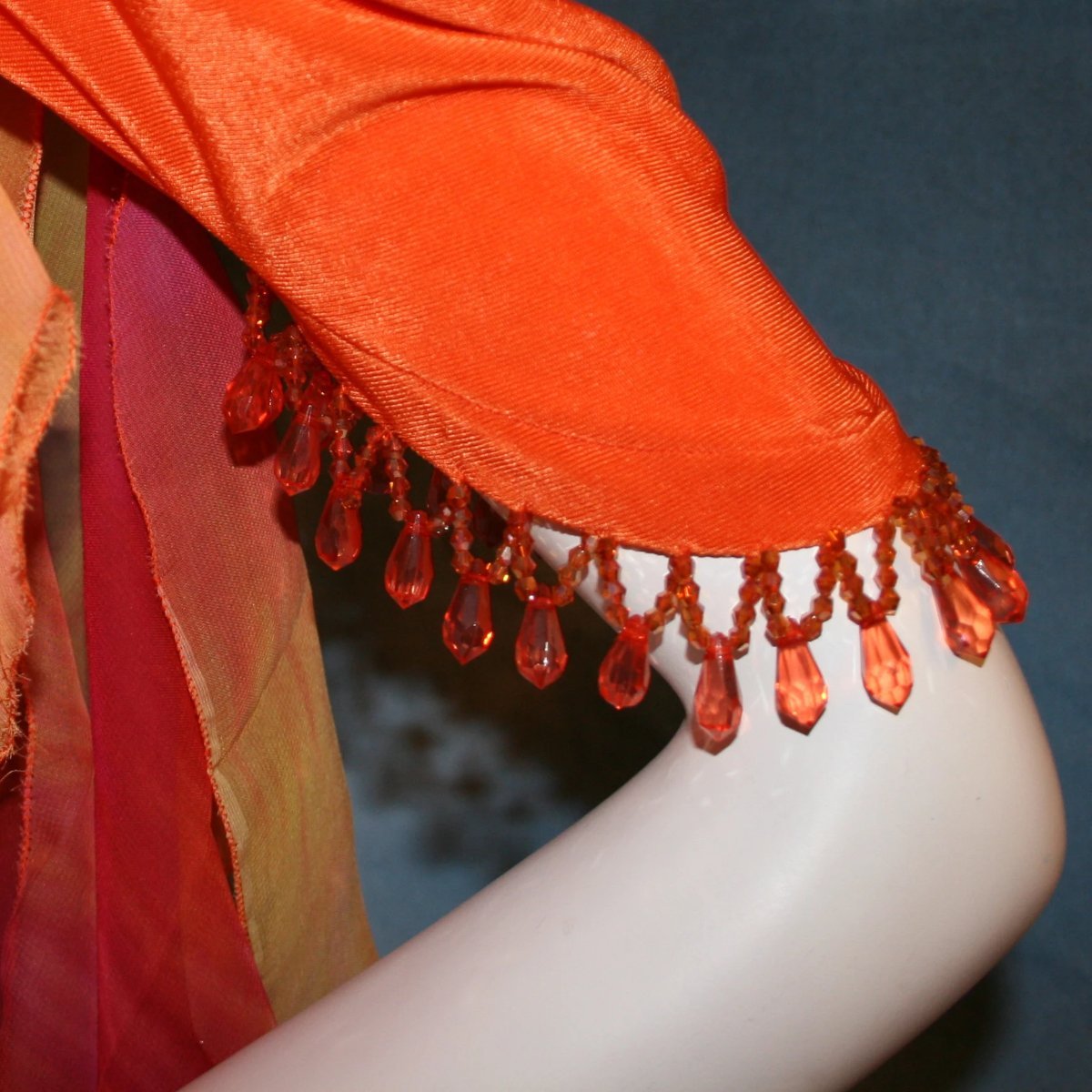 arm detail of Orange social ballroom dress created in luxurious solid slinky fabric with chiffon insets of rainbow oranges & yellows, with hand beading on arm draping. Very full around bottom, and makes a great beginner ballroom dancer smooth dress.