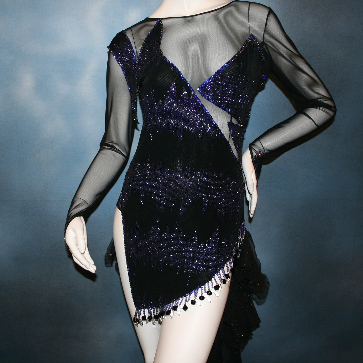 Crystal's Creations Close up view of Latin/rhythm/tango dress created in black glitter slinky with an awesome electrifying tanzanite/perwinkle glitter pattern artistically placed on a black stretch mesh base, embellished with crystal heliotrope Preciosa rhinestone work, hand beading & features flounces in the back skirting.