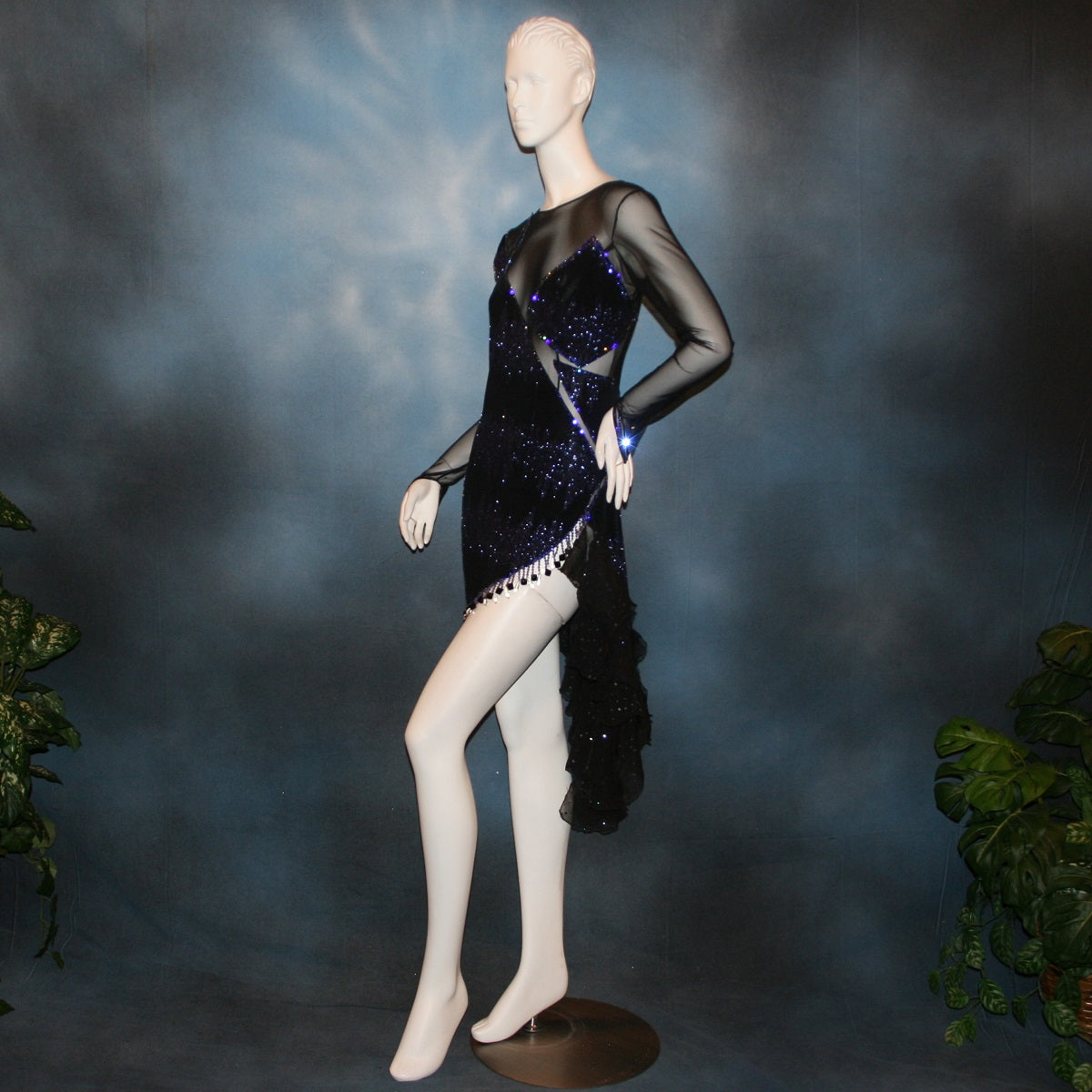 Crystal's Creations left sdie view of Latin/rhythm/tango dress created in black glitter slinky with an awesome electrifying tanzanite/perwinkle glitter pattern artistically placed on a black stretch mesh base, embellished with crystal heliotrope Preciosa rhinestone work, hand beading & features flounces in the back skirting.