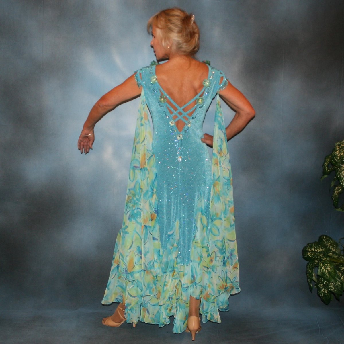Crystal's Creations back view of Turquoise ballroom dress of turquoise glitter slinky features lattice work detailing with yards & yards of print chiffon, enhanced with velveteen flowers plus aquamarine Swarovski rhinestones, hand beading on shoulder detailing... with detachable floats.