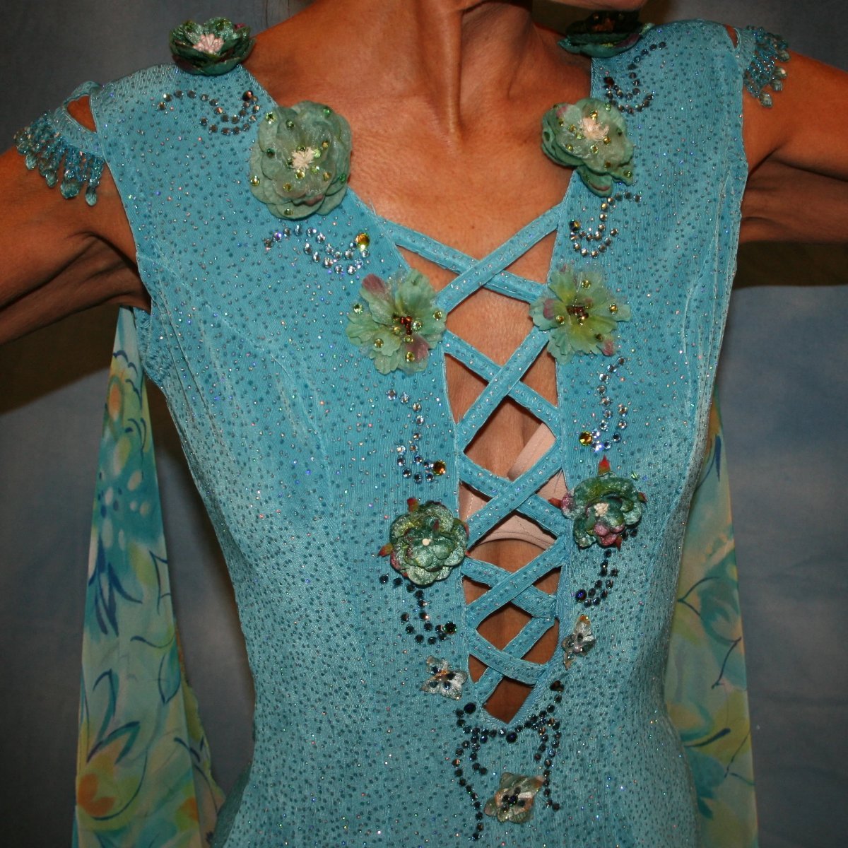 Crystal's Creations close up view of Turquoise ballroom dress of turquoise glitter slinky features lattice work detailing with yards & yards of print chiffon, enhanced with velveteen flowers plus aquamarine Swarovski rhinestones, hand beading on shoulder detailing... with detachable floats.