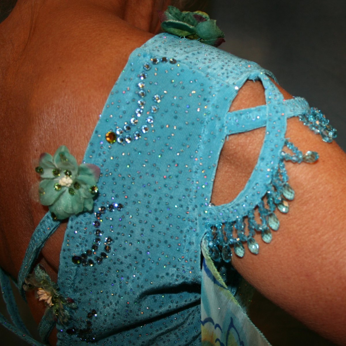 Crystal's Creations close up view of shoulder details on Turquoise ballroom dress of turquoise glitter slinky features lattice work detailing with yards & yards of print chiffon, enhanced with velveteen flowers plus aquamarine Swarovski rhinestones, hand beading on shoulder detailing... with detachable floats.