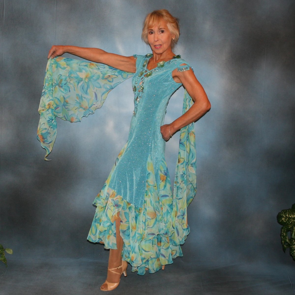 Crystal's Creations side view of Turquoise ballroom dress of turquoise glitter slinky features lattice work detailing with yards & yards of print chiffon, enhanced with velveteen flowers plus aquamarine Swarovski rhinestones, hand beading on shoulder detailing... with detachable floats.