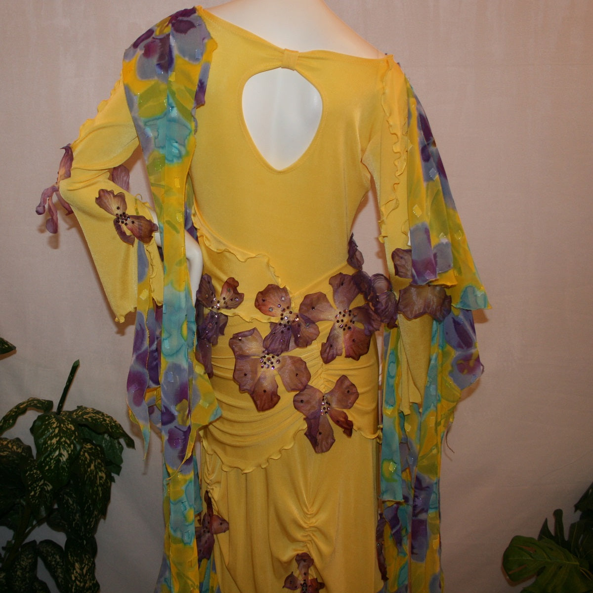 Crystal's Creations upper back view of Yellow ballroom dress created of luxurious yellow slinky with yards of flower printed textured chiffon of yellow, orchids & blues is embellished with deep orchid silk flowers that have rhinestone work in shades of orchid.