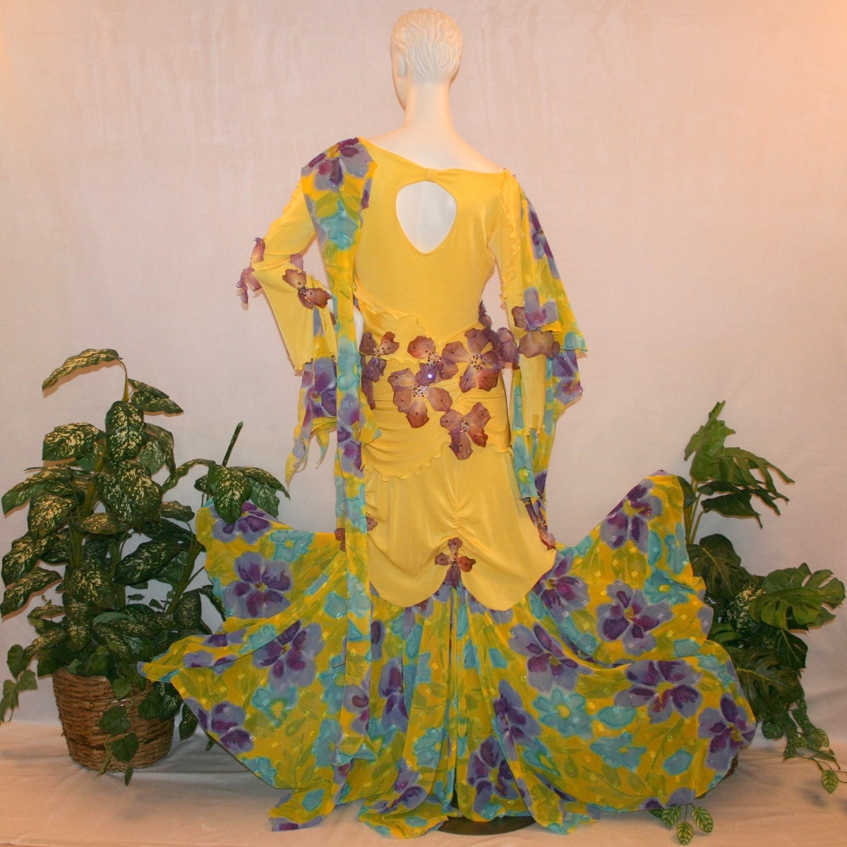 Crystal's Creations back view of Yellow ballroom dress created of luxurious yellow slinky with yards of flower printed textured chiffon of yellow, orchids & blues is embellished with deep orchid silk flowers that have rhinestone work in shades of orchid