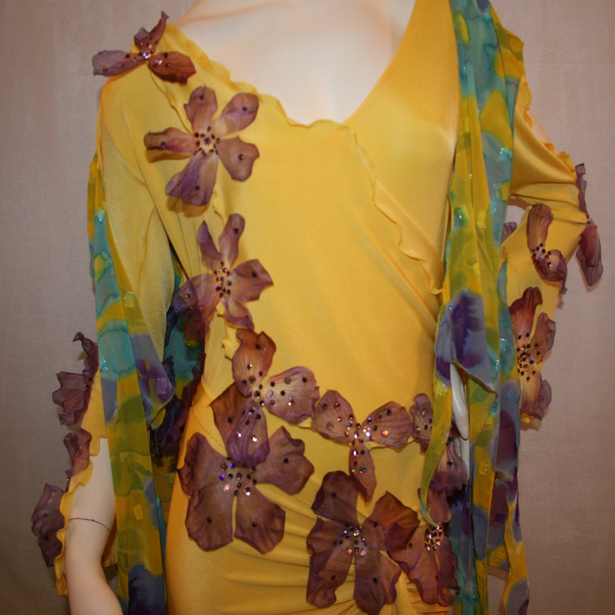 Crystal's Creations top view of Yellow ballroom dress created of luxurious yellow slinky with yards of flower printed textured chiffon of yellow, orchids & blues is embellished with deep orchid silk flowers that have rhinestone work in shades of orchid.