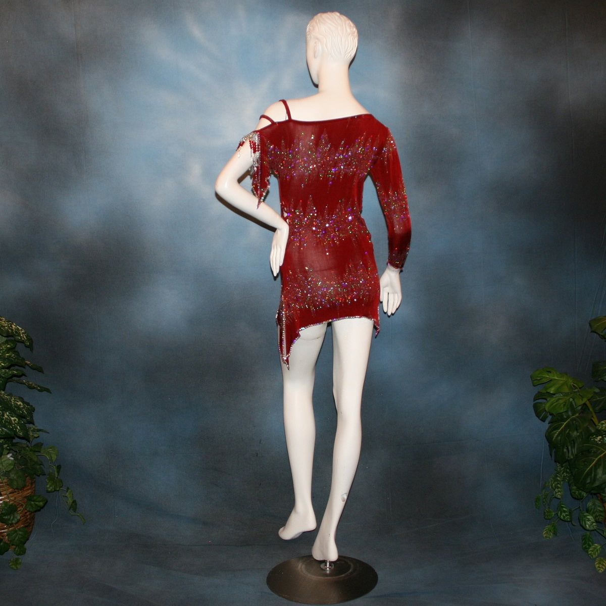 back view of Deep scarlette red Latin rhythm dress created in glitter slinky with an awesome electrifying glitter pattern features lattice detailing in the sides, one long sleeve & interesting detailing on the opposite shoulder with Swarovski hand beading & Crystal Ab rhinestone work edging the skirting, split cape sleeve & long sleeve.