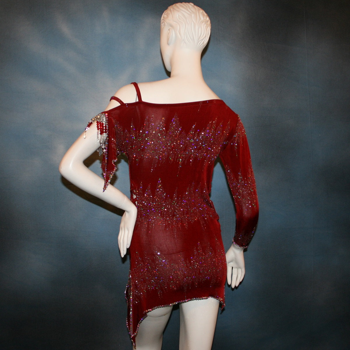 close back view of Deep scarlette red Latin rhythm dress created in glitter slinky with an awesome electrifying glitter pattern features lattice detailing in the sides, one long sleeve & interesting detailing on the opposite shoulder with Swarovski hand beading & Crystal Ab rhinestone work edging the skirting, split cape sleeve & long sleeve.