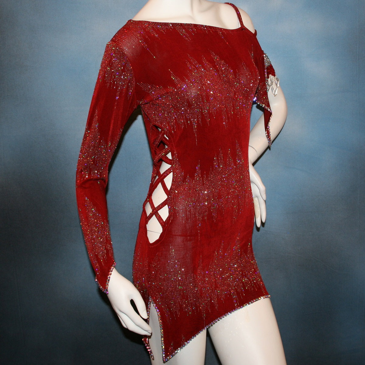 close right side view of Deep scarlette red Latin rhythm dress created in glitter slinky with an awesome electrifying glitter pattern features lattice detailing in the sides, one long sleeve & interesting detailing on the opposite shoulder with Swarovski hand beading & Crystal Ab rhinestone work edging the skirting, split cape sleeve & long sleeve.
