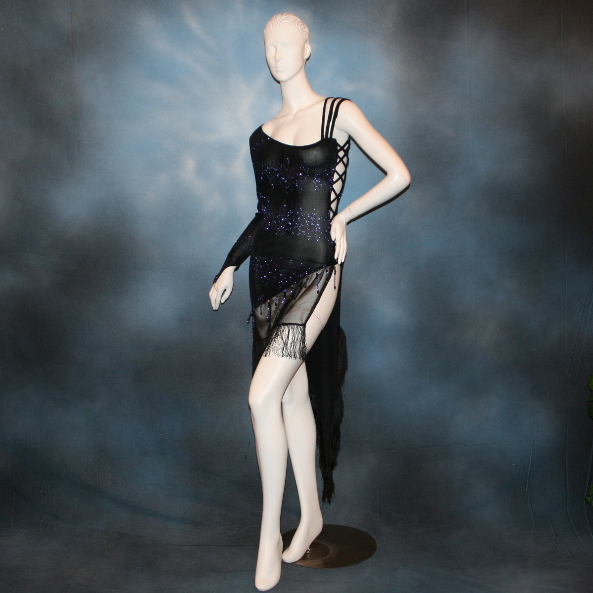 Latin/rhythm/tango dress created in black glitter slinky with an awesome electrifying tanzinite/perwinkle glitter pattern! It features one long sleeve, lattice work detailing up the left side, a short skirt line in front that angles down to a long peak in the back, with a sheer mesh inset, fringe & Swarovski hand beading in tanzanite & black.