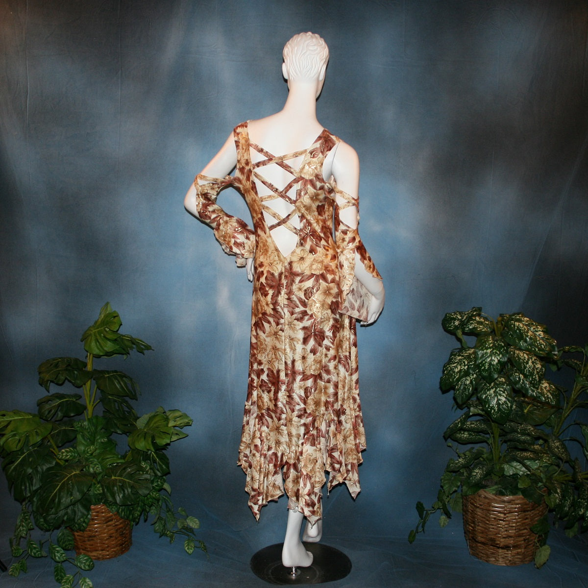 back view of Ballroom social dress created of brown tropical print lycra with shiny gold accents through the print, features low back & cold shoulder 3/4 sleeves with flounces & lattice strap details, & lots of flounces through the full skirting