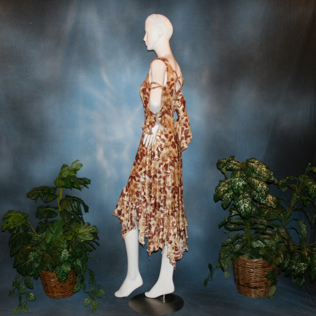 side view of Ballroom social dress created of brown tropical print lycra with shiny gold accents through the print, features low back & cold shoulder 3/4 sleeves with flounces & lattice strap details, & lots of flounces through the full skirting