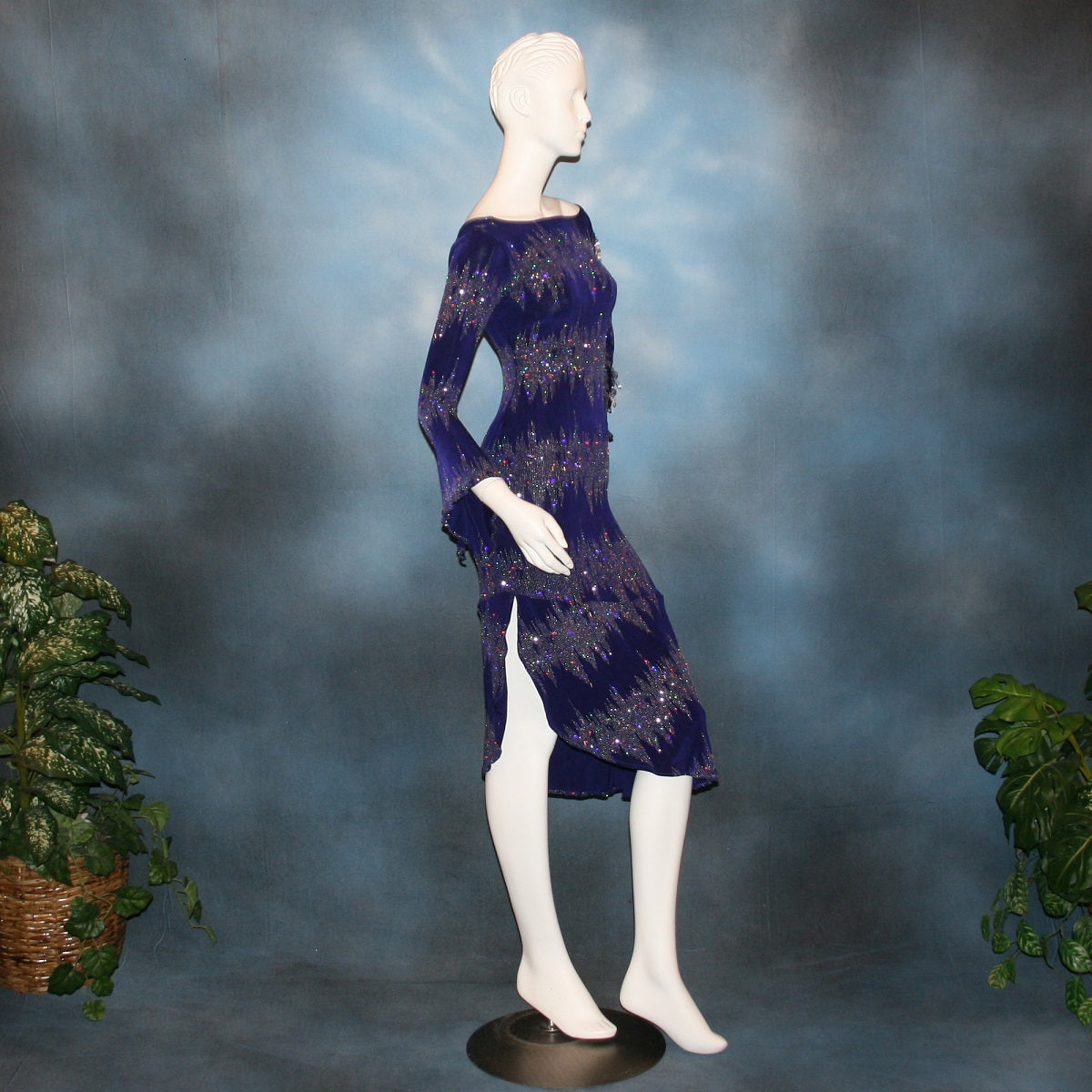 right side view of Deep royal purple Latin/rhythm/tango dress created in deep royal purple glitter slinky with an awesome electrifying glitter pattern features one longe sleeve, with flair at the bottom, & another very interesting cold shoulder detailed one with hand beading & a flaired flounce.